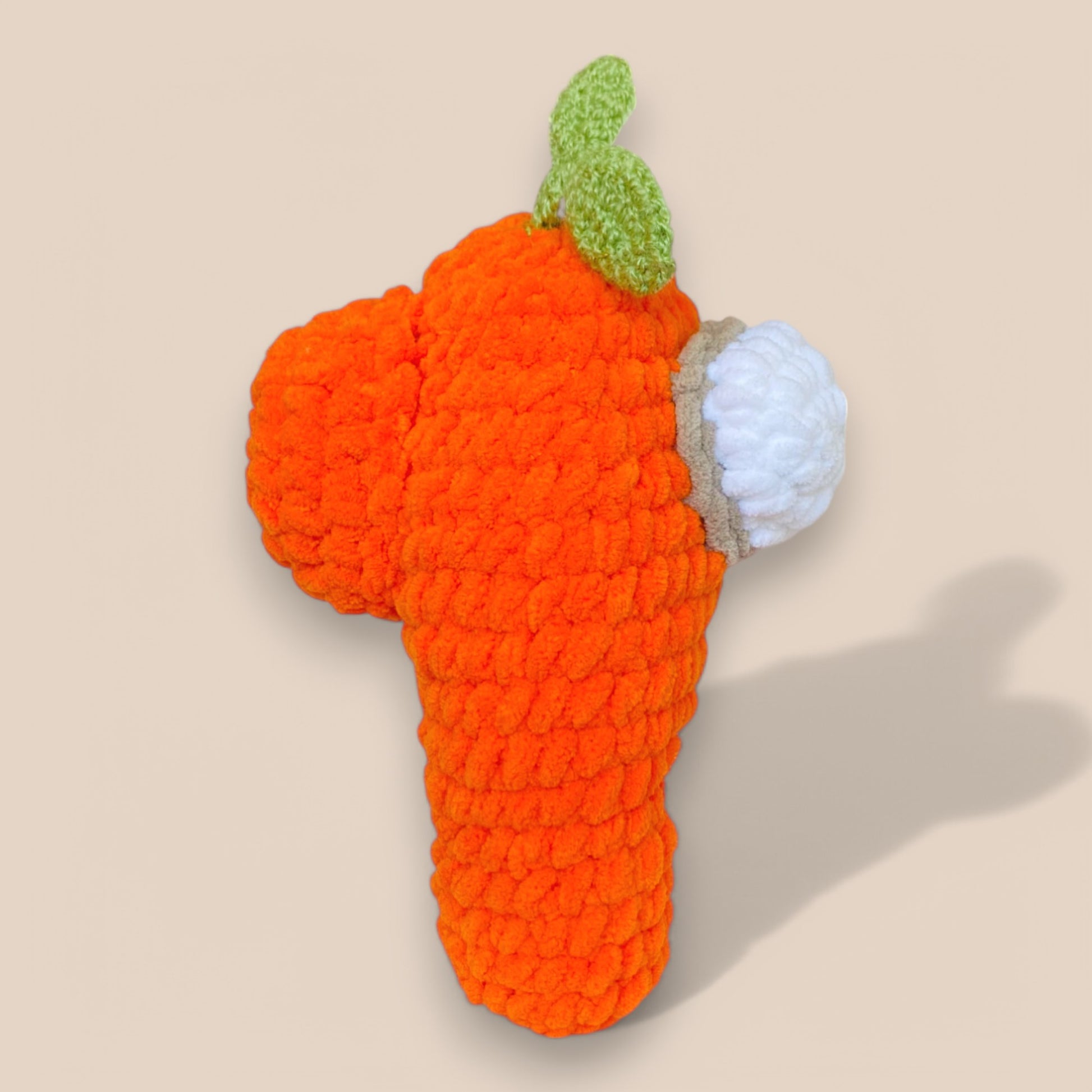 Orange handcrafted crochet toy with white face and greenleaf on top side view