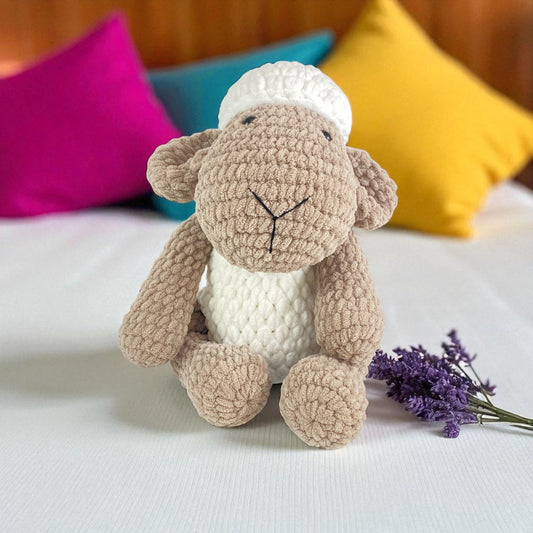 Crocheted sheep toy on a white surface with colorful pillows in the background