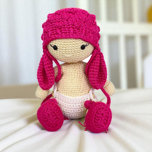 Crocheted doll with pink mouse cap and a  sitting on a white surface.