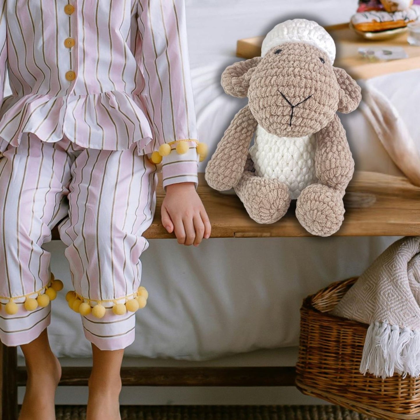 Child in striped pajamas holding a knitted sheep toy on a bed.