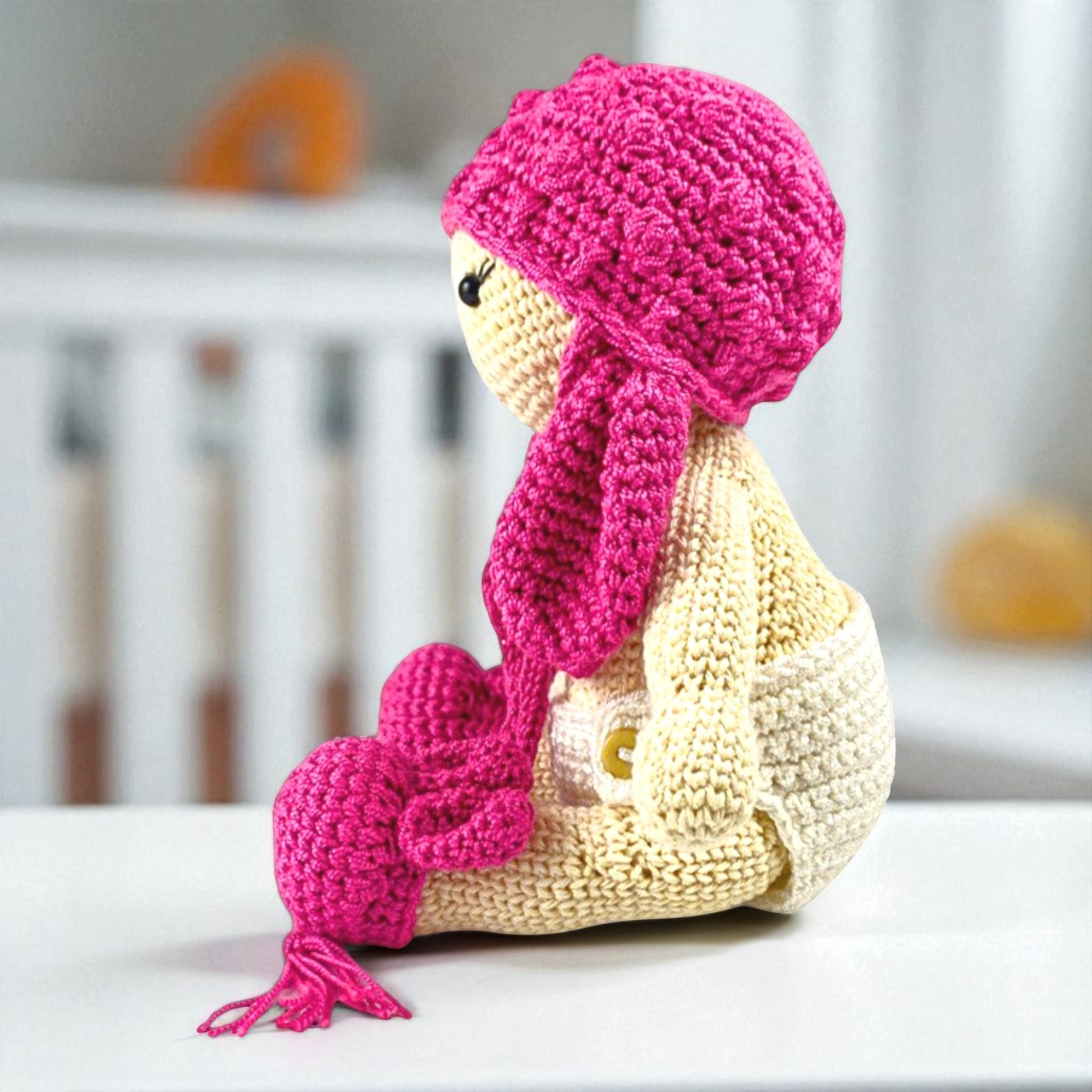 Crocheted toy with pink hat and scarf on a white surface