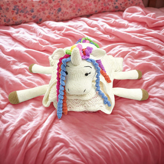 a handmade crochet white blanket converts as unicorn with rainbow mane when folded .kept on pink bedsheet,